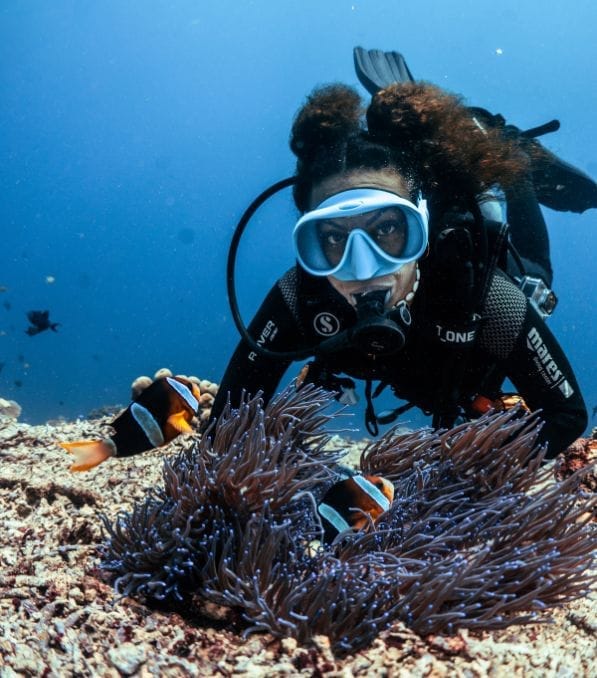Scuba diver at Nusa Penida hovering over a reef, watching clownfish sheltering in a sea anemone.