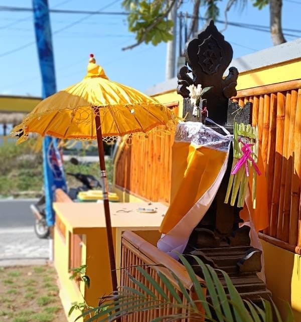 Small shrine on Nusa Penida decorated with a yellow umbrella, cloth sash and woven palm offerings at the roadside.