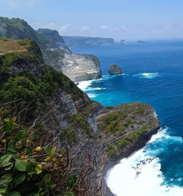 Nusa Penida cliffs with waves crashing against rocky headlands and turquoise sea under a clear blue sky