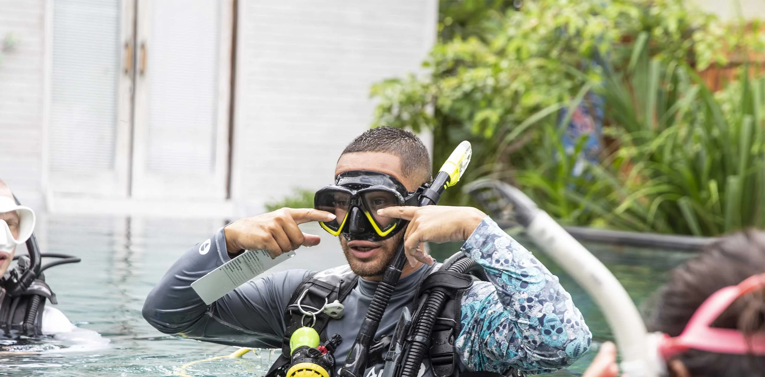 Discover-Scuba-Diving-Penida Scuba instructor in Nusa Penida adjusts his dive mask and demonstrates snorkel and regulator skills to students in a pool.