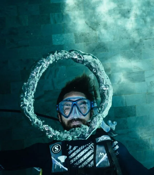 Scuba diver in Nusa Penida underwater blowing a large circular air bubble ring around his masked face.