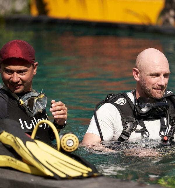 scuba-diving-penida 2 Two scuba divers preparing to dive in Nusa Penida waters, adjusting their gear with fins and a regulator nearby.