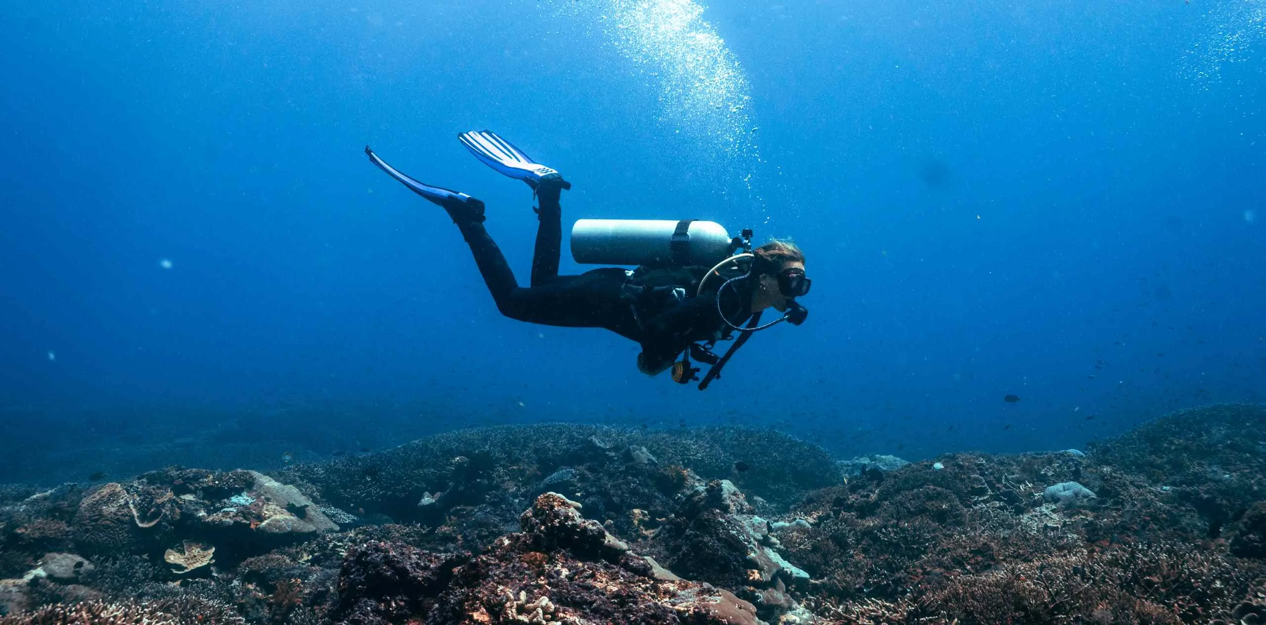 Scuba diver exploring a coral reef off Nusa Penida, swimming above the seabed with bubbles rising.