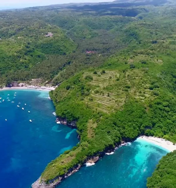 An Island Bursting with Adventures 3 Aerial view of Nusa Penida showing turquoise bays, white-sand beaches, anchored boats and terraced green hills.
