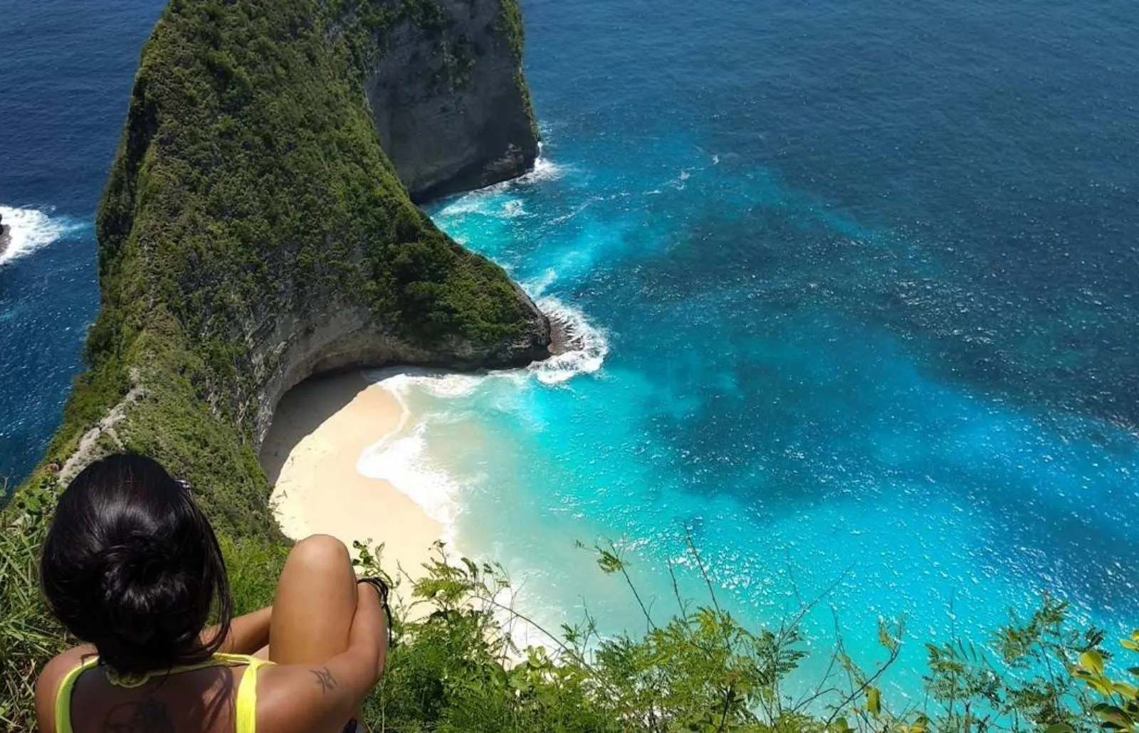 Nusa Penida_ An Island Bursting with Adventures Person sits on a cliff edge overlooking the turquoise bay and sandy cove at Nusa Penida.